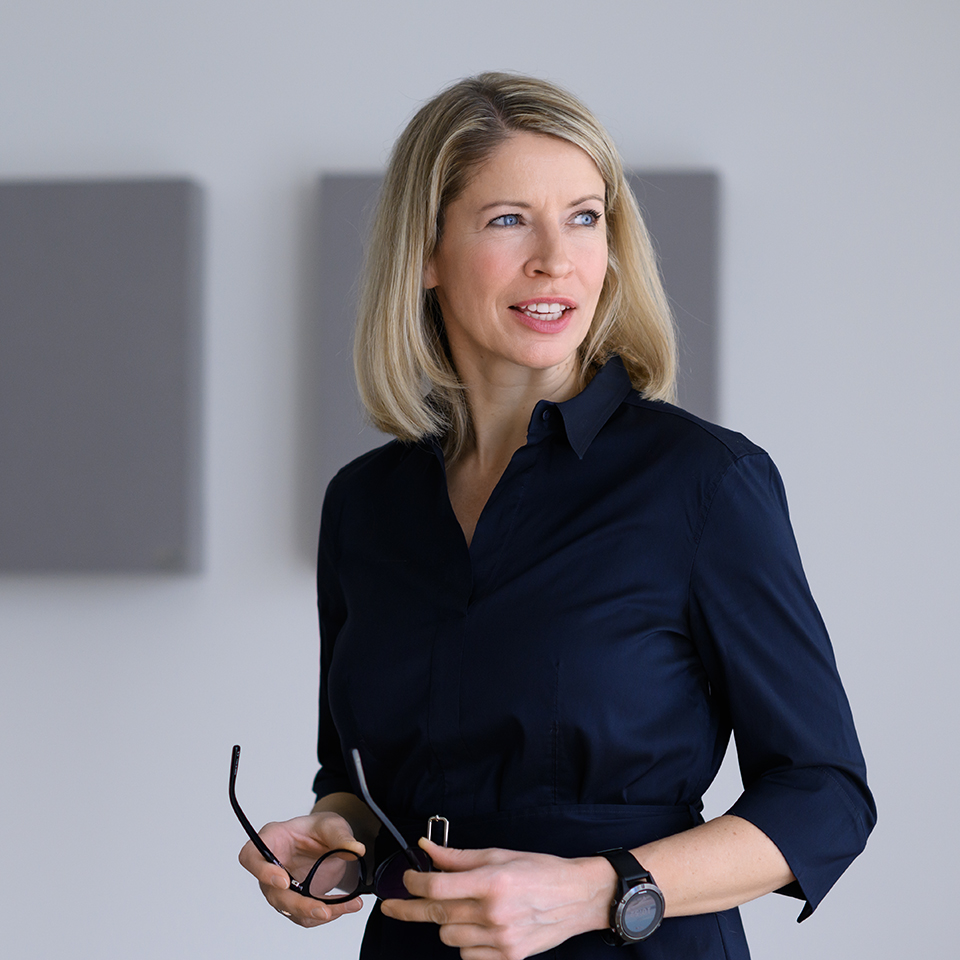 Confident businesswoman in a dark shirt, holding her eyeglasses, and gazing thoughtfully